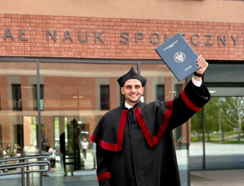 Jakub Klepański pozuje z pracą doktorską przed Wydziałem Nauk Społecznych 
