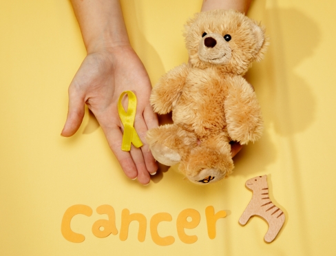 Zdjęcie ilustracyjne z napisem "cancer" przedstawia misia i dłoń, na której leży złota wstążką