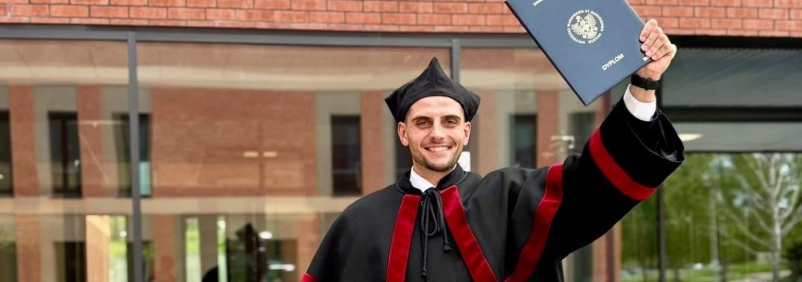 Jakub Klepański pozuje z pracą doktorską przed Wydziałem Nauk Społecznych 